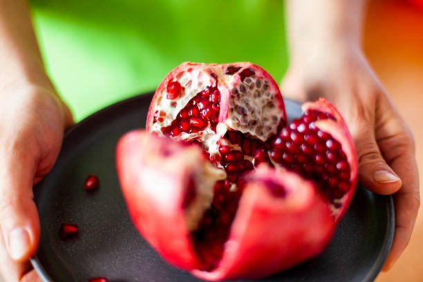 Woman hands with ripe pomegranate fruit on gray plate. Close-up